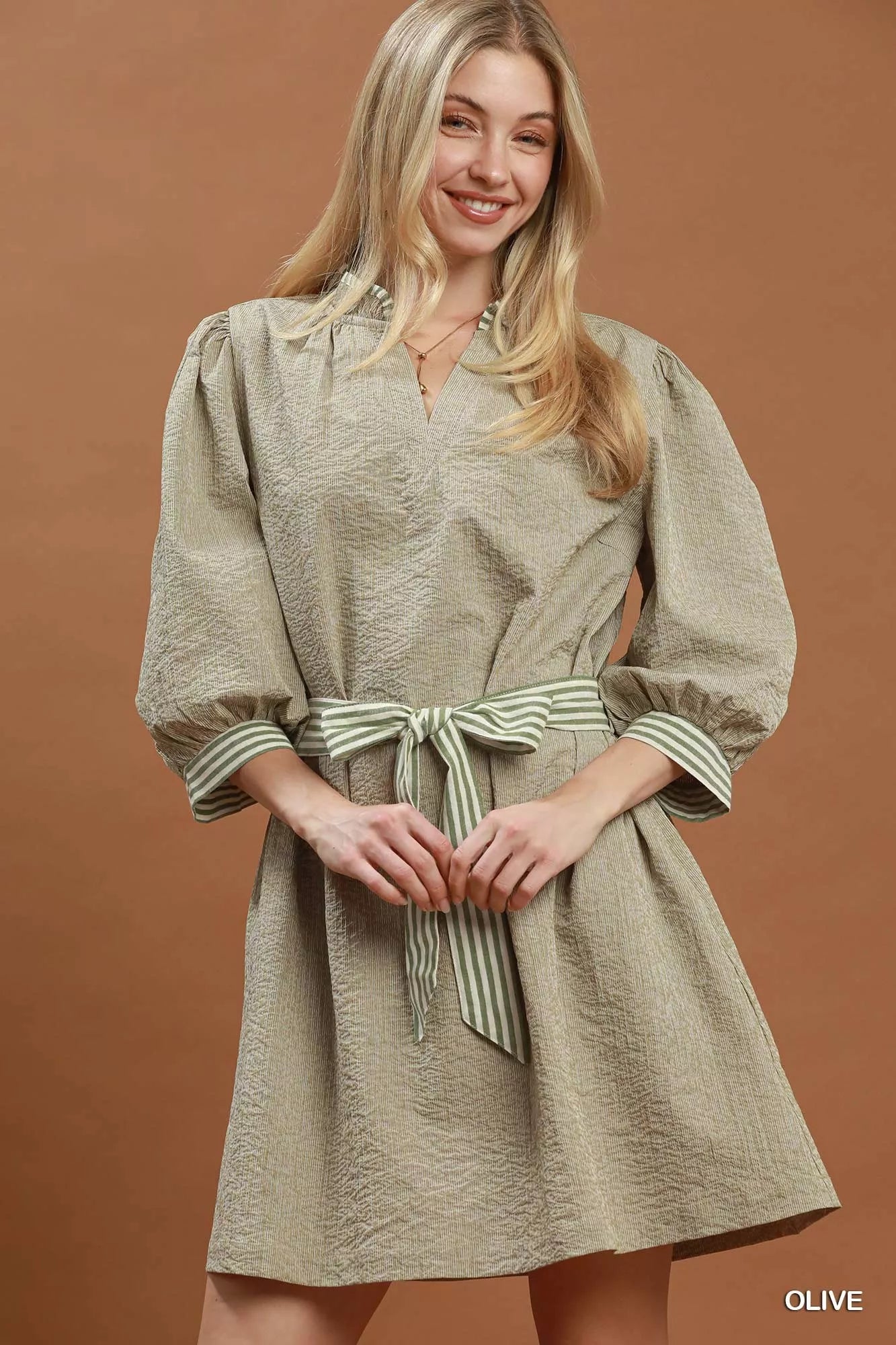 Woman wearing Umgee olive textured contrast trim tie waist mini dress with striped belt and puff sleeves.